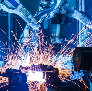 Two robotic arms in an industrial setting with sparks flying