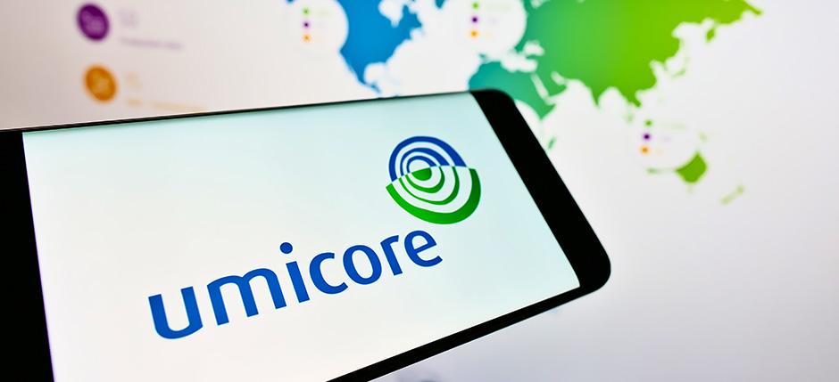 A cell phone displaying the Umicore logo in front of a computer showing a map of company locations.